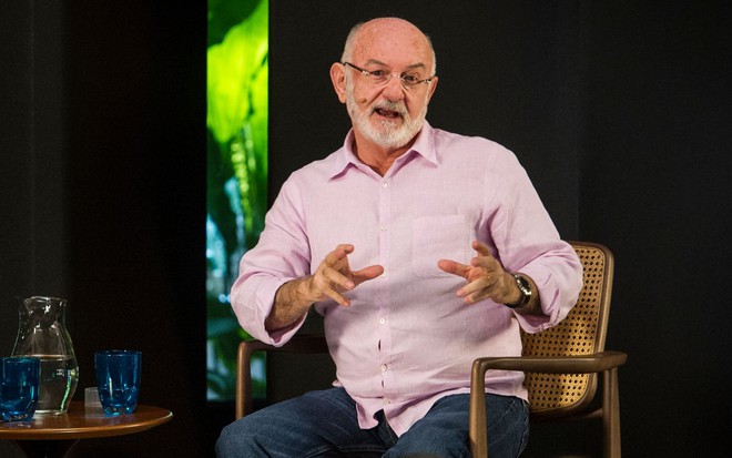 Silvio de Abreu em entrevista à GloboNews em 2019; ele veste camisa cor de rosa à frente de cenário escuro