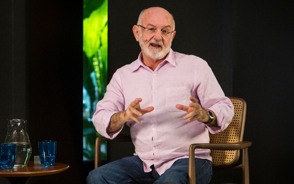 Silvio de Abreu em entrevista à GloboNews em 2019; ele veste camisa cor de rosa à frente de cenário escuro