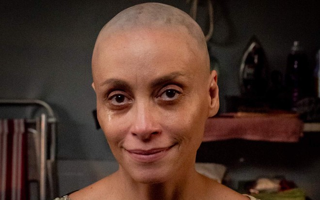 A atriz Suzana Pires com leve sorriso de boca fechada, careca, em cena do filme Câncer com Ascendente em Virgem