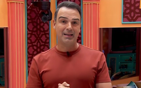 Foto mostra Tadeu Schmidt durante Big Brother Brasil; ele veste camiseta laranja