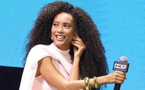 A atriz Taís Araujo sorrindo com microfone na mão, durante painel na CCXP