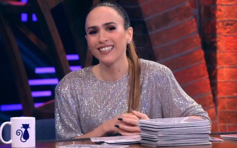 Tatá Werneck está sentada em uma mesa, no cenário do Lady Night, com fichas e uma caneca à sua frente