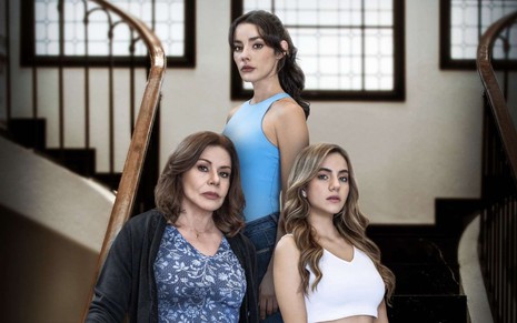 Três mulheres, uma mais velha e duas jovens, posam em uma escadaria com expressões sérias