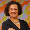 Maria Angela de Jesus posa sorridente, com os braços cruzados, na frente de um fundo colorido