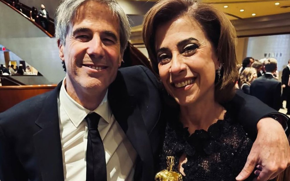 Walter Salles e Fernanda Torres lado a lado, sorridentes, enquanto a atriz segura a estatueta do Oscar