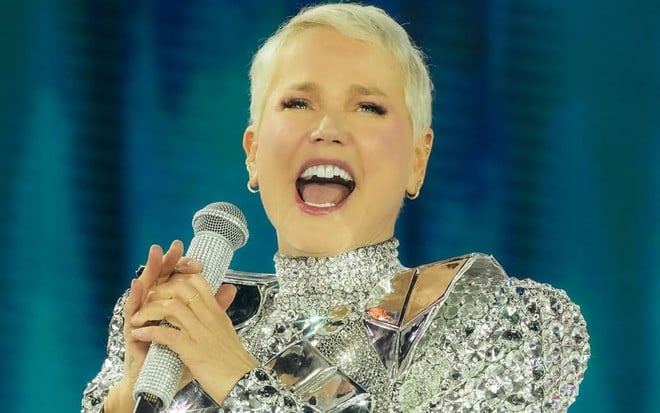 mulher loira canta em show; ela veste roupa prateada brilhante