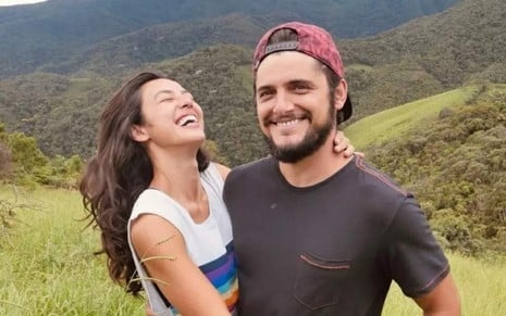 Os atores Yanna Lavigne e Bruno Gissoni abraçados e sorrindo no meio do mato