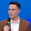 Luiz Bacci fala em microfone, com o palhaço Patatá ao fundo