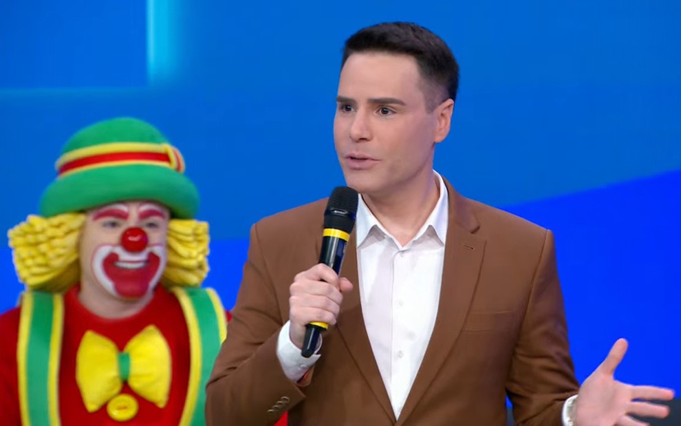 Luiz Bacci fala em microfone, com o palhaço Patatá ao fundo