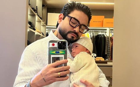 Yudi Tamashiro segurando o filho no colo e tirando uma foto no espelho