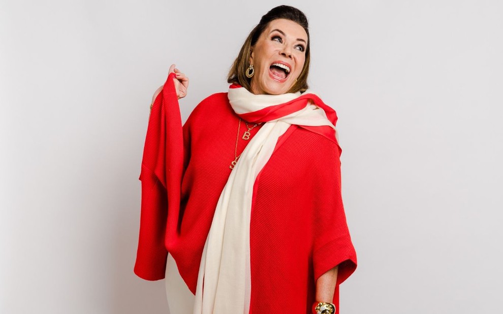 Beth Szafir esbanja felicidade com a boca aberta e vestindo uma blusa vermelha em imagem de divulgação do reality show Os Szafir