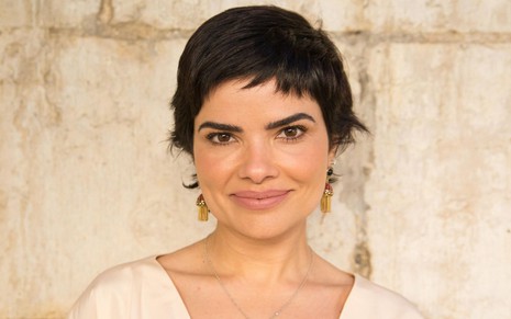 Vanessa Giácomo sorri discretamente e está com os cabelos curtos, caracterizada como Leonor na novela Travessia (2022)