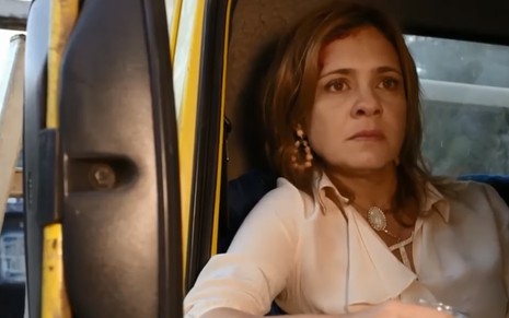 A atriz Adriana Esteves caracterizada como a Carminha de Avenida Brasil, sentada na boleia de um caminhão de lixo, com um copo de aguardente na mão