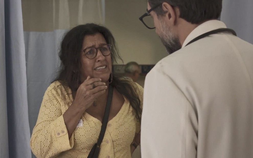 A atriz Regina Casé caracterizada como a Lurdes em cena de Amor de Mãe, ela olha para um médico com rosto horrorizado