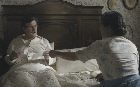 O ator Antonio Calloni caracterizado como o Júlio de Éramos Seis, acamado, recebe um documento das mãos de Lola, interpretada por Gloria Pires