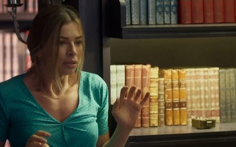 Grazi Massafera em cena da novela Bom Sucesso como a personagem Paloma, com uma estante de livros atrás dela 