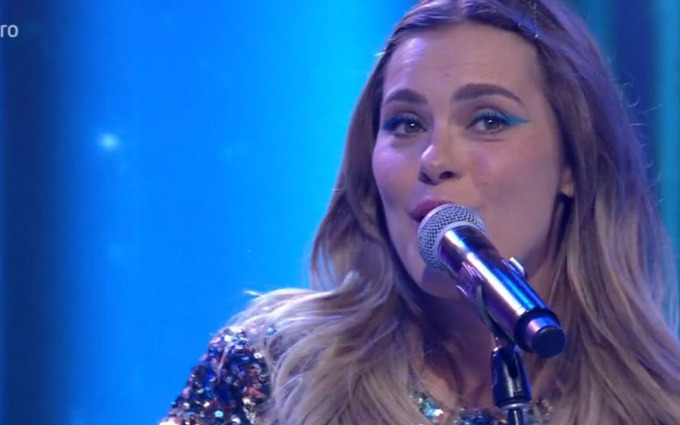 A atriz Carolina Dieckmann cantando na frente de um microfone no palco do programa Encontro com Fátima Bernardes