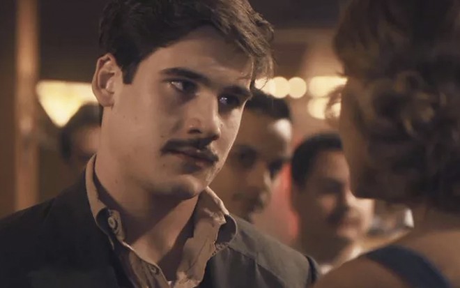 O ator Nicolas Prattes caracterizado como o Alfredo de Éramos Seis, olha para Ellen Rocche, a Marion, que está de costas