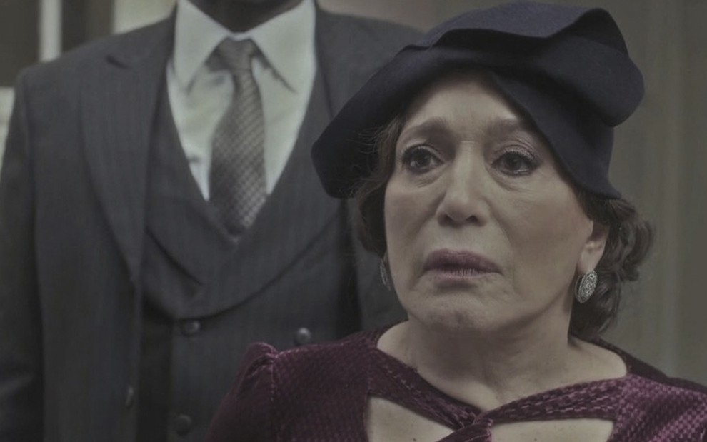 A atriz Susana Vieira caracterizada como a personagem Emília, com um chapéu preto e uma roupa vinho, em cena de Éramos Seis