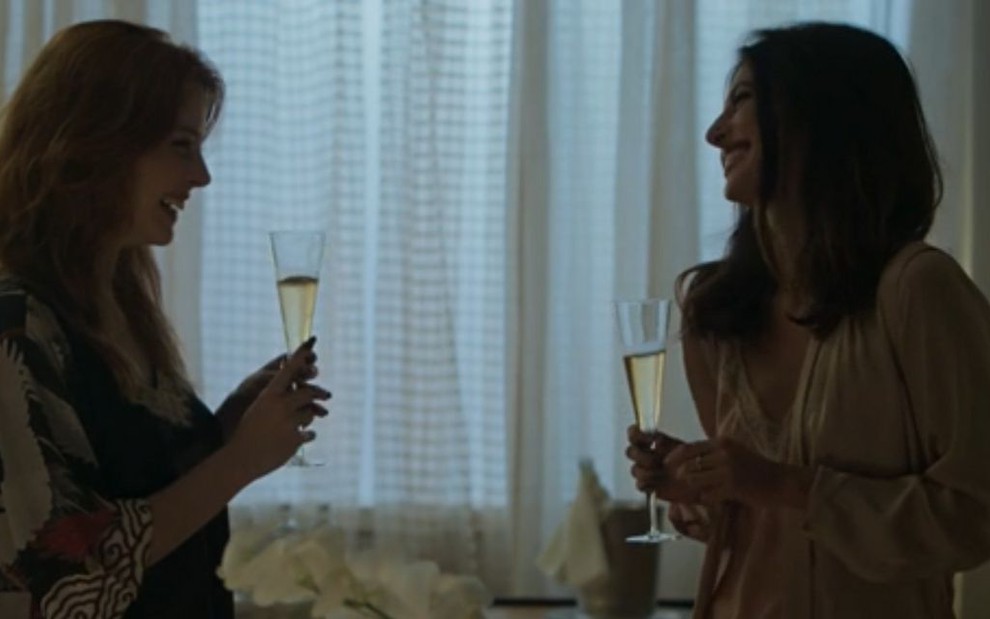 Atrizes Bia Arantes e Anaju Dorigon em cena como as personagens Valéria e Camila, respectivamente, segurando taças de champanhe na novela Órfãos da Terra, da Globo