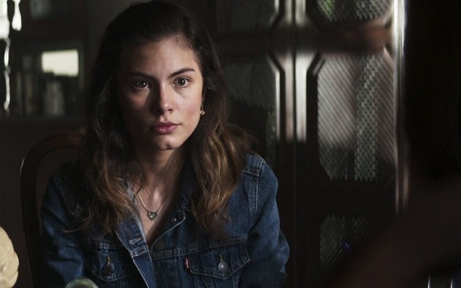 A atriz Bruna Hamú caracterizada como a Joana em A Dona do Pedaço, sentada em uma cadeira