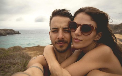 Junior Lima e sua mulher, Monica Benini, na praia. O cantor está sem camisa e Monica está abraçada em seus ombros e usando óculos escuros