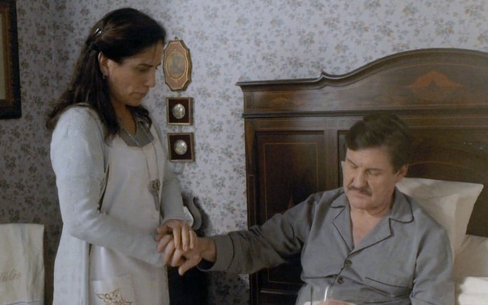 A atriz Gloria Pires caracterizada como Lola e o ator Antonio Calloni, na pele de Júlio, está na cama com um copo de leite na mão