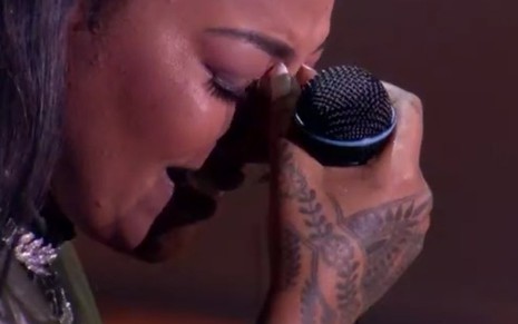 A cantora Ludmilla chora com um microfone na mão no palco do Prêmio Multishow