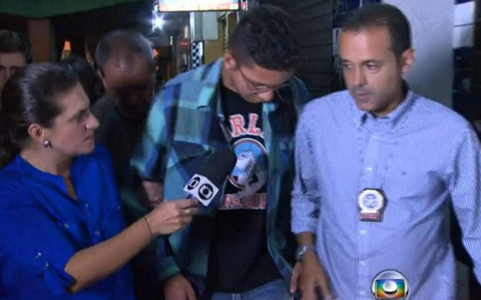 A repórter Bette Lucchese entrevista Caio Silva de Souza observada por policial do Rio de Janeiro - Reprodução/TV Globo
