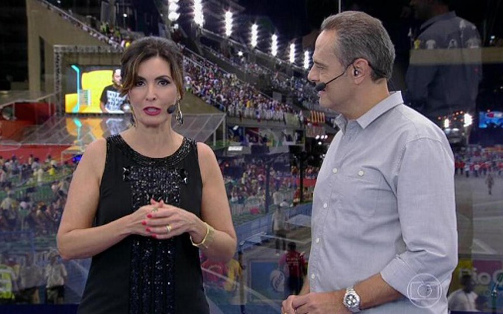 Fátima Bernardes e Luís Roberto gravam transmissão como se fosse ao vivo; ao fundo, telão exibia BBB - Reprodução/TV Globo