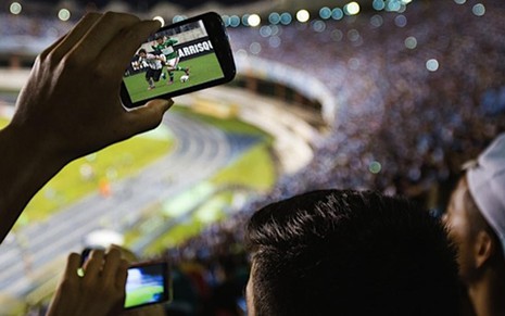Torcedor acompanha partida de futebol em estádio com celular sintonizado na TV - Divulgação