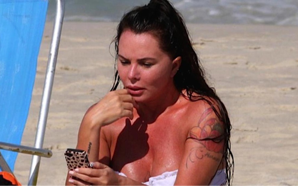 A ex-modelo Cristina Mortágua confere mensagens em celular na praia da Barra da Tijuca, em junho - Wallace Barbosa/AgNews