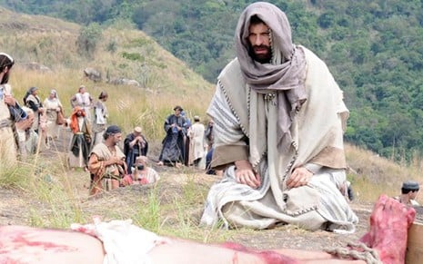 O ator Milhem Cortaz, como Barzilai, se ajoelha e vê 'Jesus Cristo' crucificado em minissérie da Record - Divulgação/TV Record