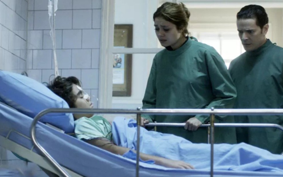 Alice (Sophie Charlotee) e Vitor (Daniel de Oliveira) choram no leito de Lucas (Xande Valois) - Reprodução/TV Globo