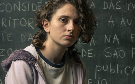 A atriz Carol Duarte em sala de aula, cenário da série Segunda Chamada, caracterizada como a personagem Solange