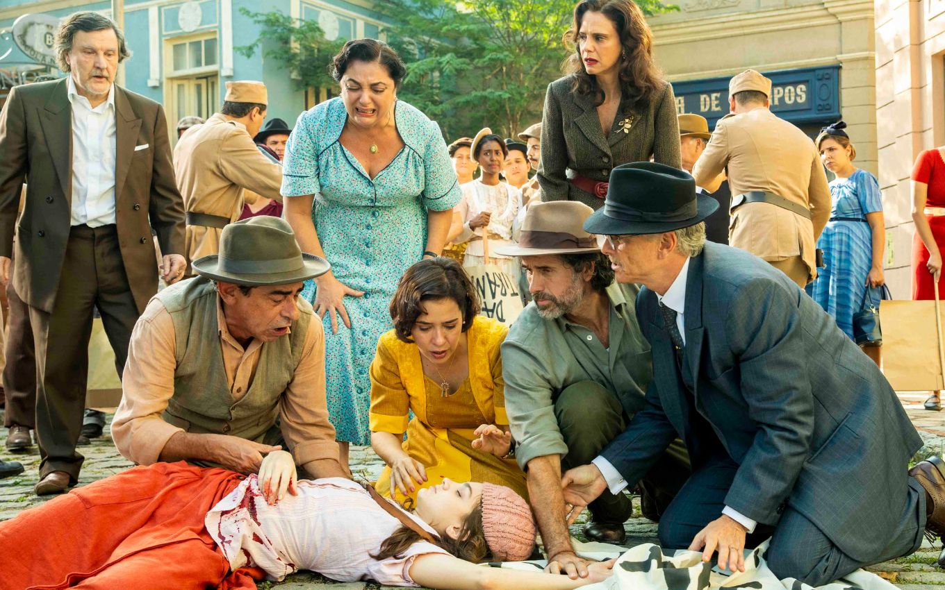 Debora Ozório caída no chão e rodeada por outros atores