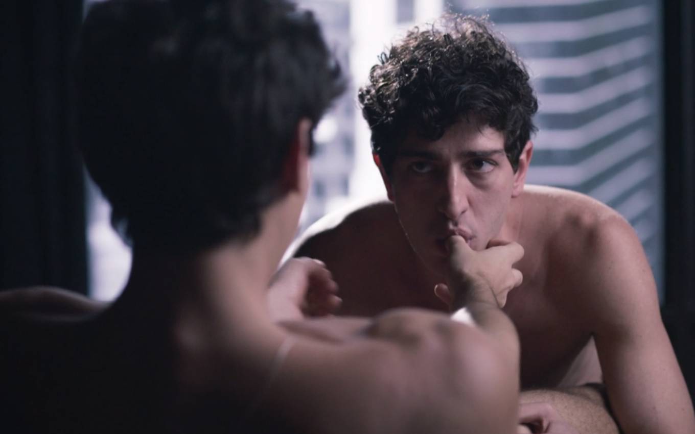 Nu, o ator Bruno Montaleone como Mateus, de costas, tem o dedo polegar da mão direita chupado pelo ator Johnny Massaro, o Giotto, em cena de Verdades Secretas 2