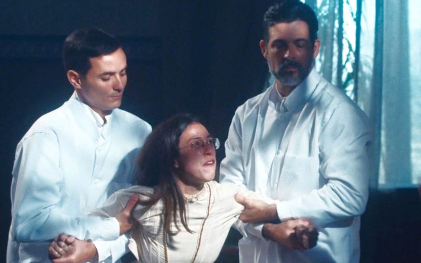 A atriz Daphne Bozaski como Dolores é contida por dois enfermeiros e colocada em uma camisa de força em cena de Nos Tempos do Imperador