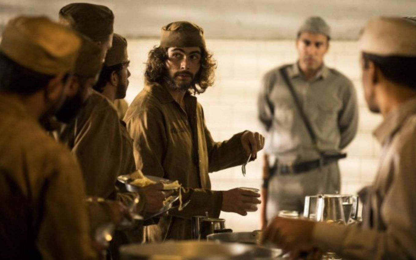 O ator Rafael Vitti como o Davi com roupas de prisioneiro na fila de um refeitório em cena de Além da Ilusão