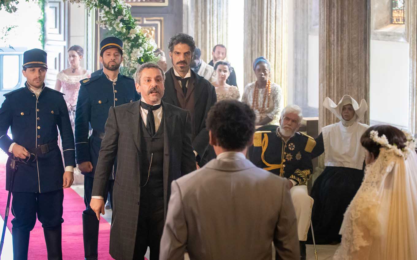 O ator Alexandre Nero como Tonico, com um grupo de policias atrás, invade uma cerimônica de casamento em cena de Nos Tempos do Imperador