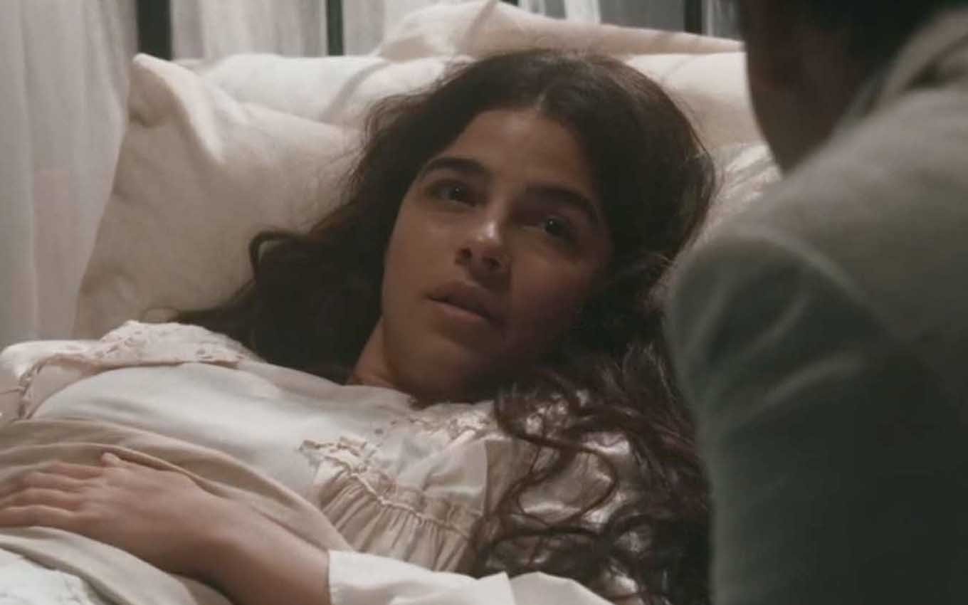 A atriz Gabriela Medvedovski caracterizada como a Pilar, em um leito de hospital, em cena de Nos Tempos do Imperador
