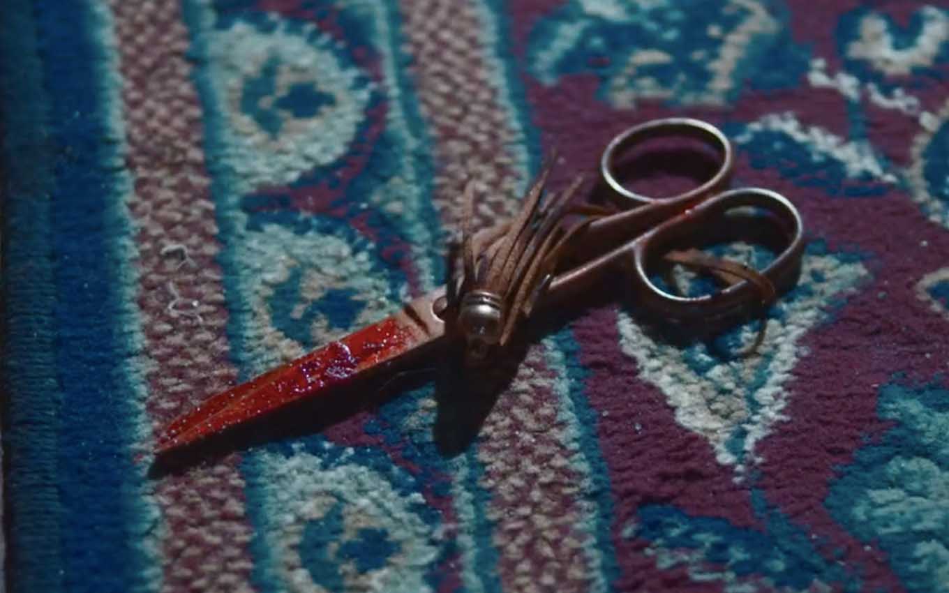 Uma tesoura ensanguentada caída em cima de um tapete com motivos persas em cena de Nos Tempos do Imperador