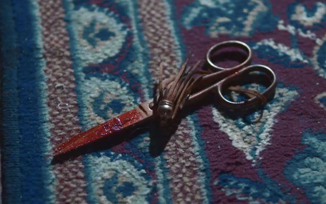Uma tesoura ensanguentada caída em cima de um tapete em cena de Nos Tempos do Imperador