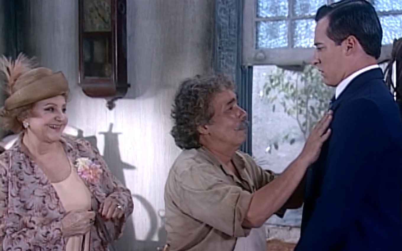 Calixto (Pedro Paulo Rangel) apoia as mãos nos ombros de Heitor (Rodrigo Faro); Josefa (Eva Todor) encara tudo admirada em cena de O Cravo e a Rosa