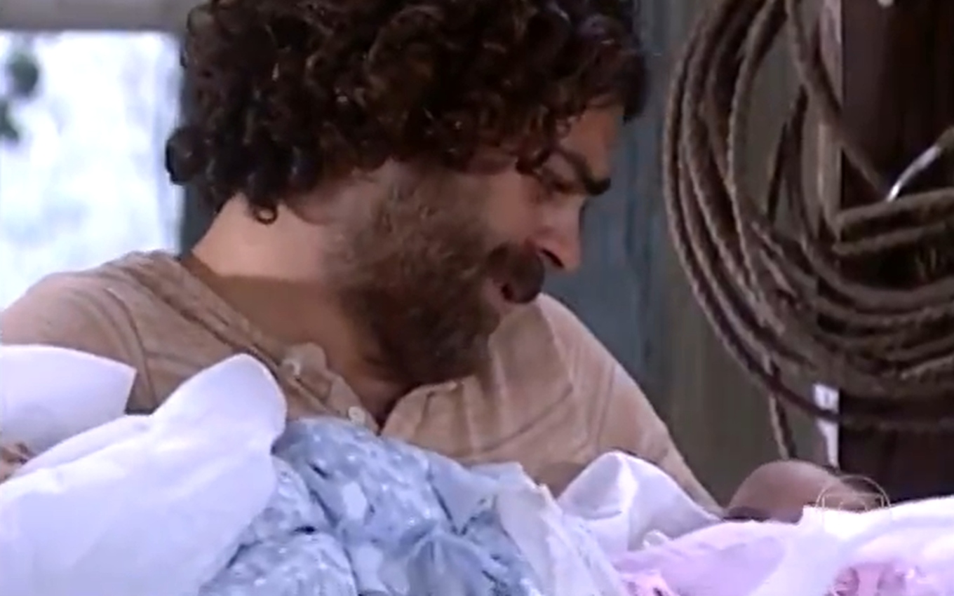 Eduardo Moscovis, caracterizado como Petruchio, segura um bebê em cada mão em cena de O Cravo e a Rosa