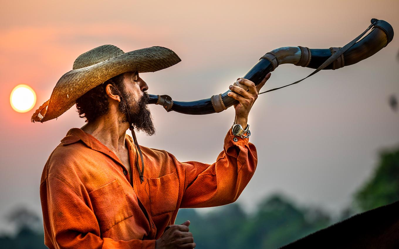 Em cima de um cavalo, Irandhir Santos como Joventino toca um berrante ao pôr do sol em Pantanal