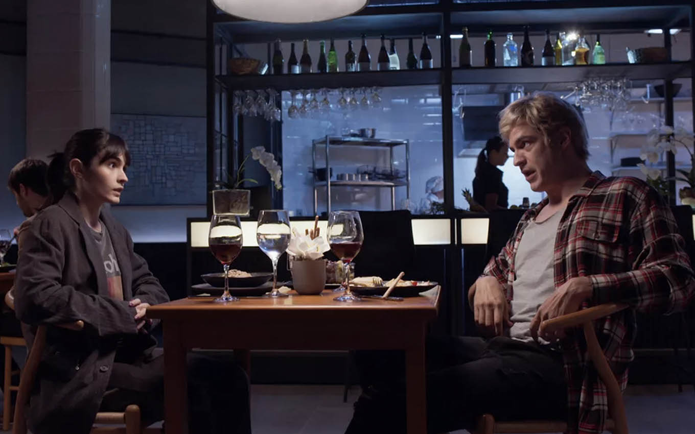 A atriz Valentina Herszage como Flávia e o ator Mateus Solano como Guilherme sentados em um bar em cena de Quanto Mais Vida, Melhor