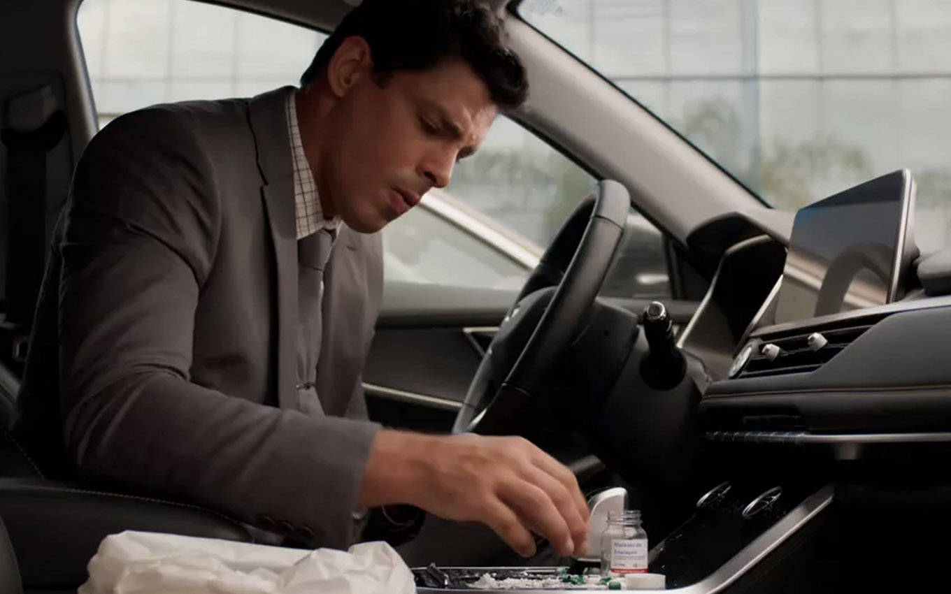 Dentro de um carro, Cauã Reymond como Christian mexe em um frasco com várias cápsulas de remédio em cena de Um Lugar ao Sol