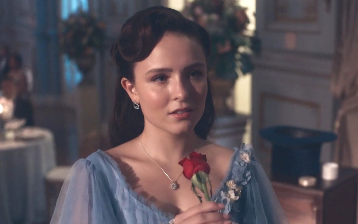 A atriz Larissa Manoela caracterizada como Elisa segura uma rosa com as mãos em cena de Além da Ilusão