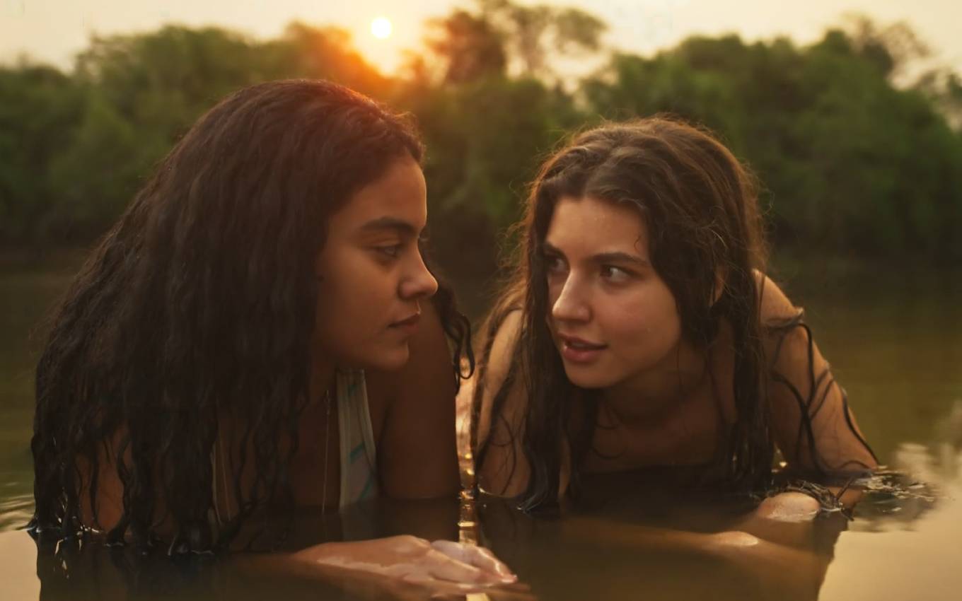 A atriz Bella Campos como Muda à esquerda deitada à margem de um rio, e a atriz Alanis Guillen como Juma à direita em cena de Pantanal